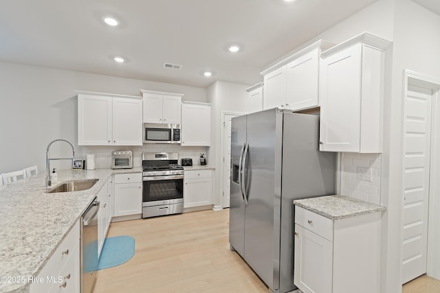 kitchen featuring sink, light stone counters, light hardwood / wood-style flooring, appliances with stainless steel finishes, and white cabinets