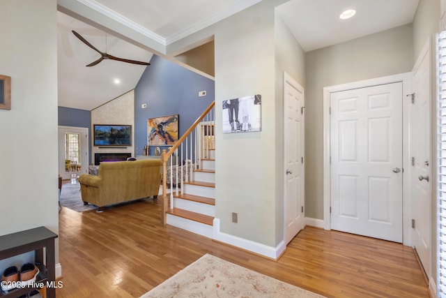 foyer entrance featuring a fireplace, hardwood / wood-style flooring, ceiling fan, high vaulted ceiling, and crown molding