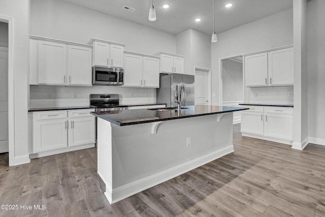 kitchen featuring white cabinetry, appliances with stainless steel finishes, an island with sink, pendant lighting, and light hardwood / wood-style floors