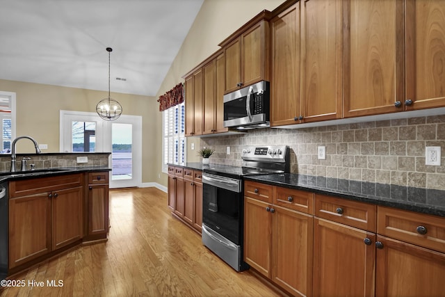 kitchen featuring lofted ceiling, appliances with stainless steel finishes, brown cabinets, light wood-type flooring, and a sink