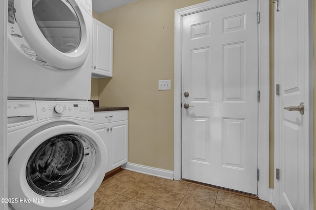 laundry room featuring cabinet space, light tile patterned floors, baseboards, and stacked washer / dryer