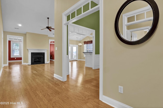 unfurnished living room with light wood finished floors, a fireplace with flush hearth, baseboards, and ceiling fan