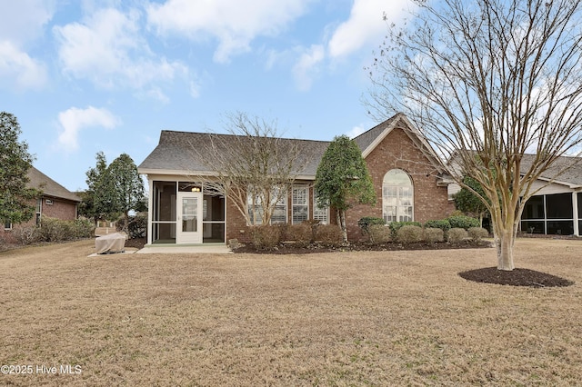 view of front of property featuring brick siding, a front yard, and a sunroom