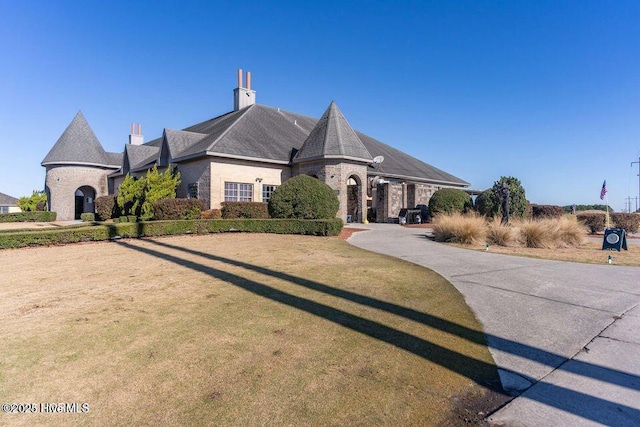 french country home with stone siding, a chimney, and a front lawn