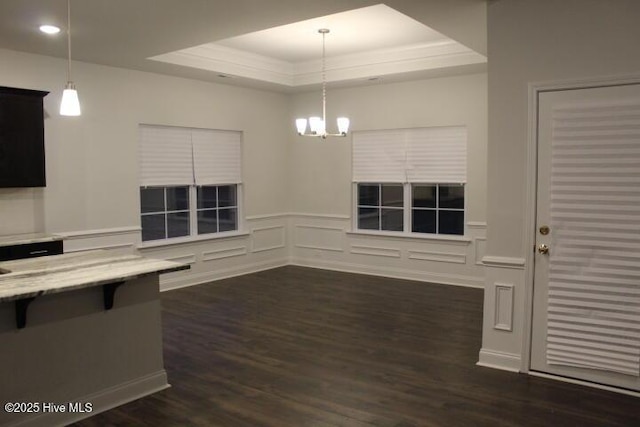 unfurnished dining area with dark hardwood / wood-style flooring, ornamental molding, a raised ceiling, and a chandelier