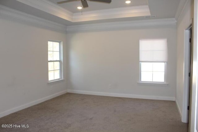 empty room with ornamental molding, light colored carpet, and a tray ceiling