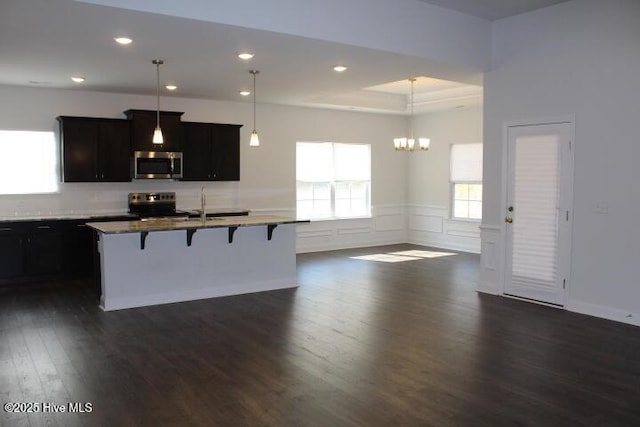 kitchen with stainless steel appliances, pendant lighting, a kitchen island with sink, and a breakfast bar area