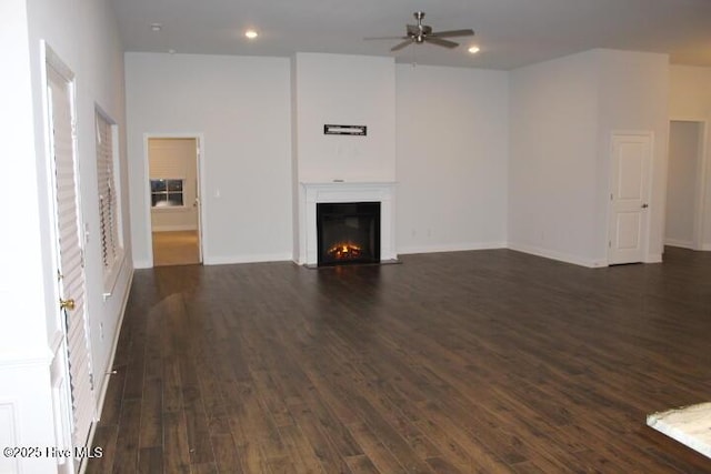 unfurnished living room with ceiling fan, a towering ceiling, and dark hardwood / wood-style flooring