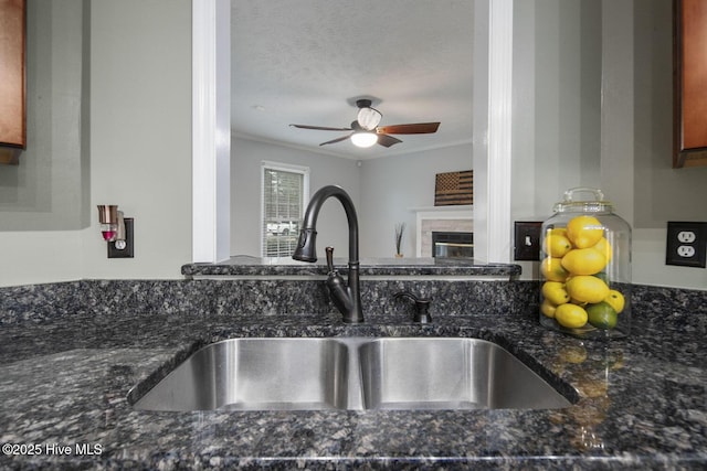 interior details with sink, a fireplace, ornamental molding, and dark stone counters