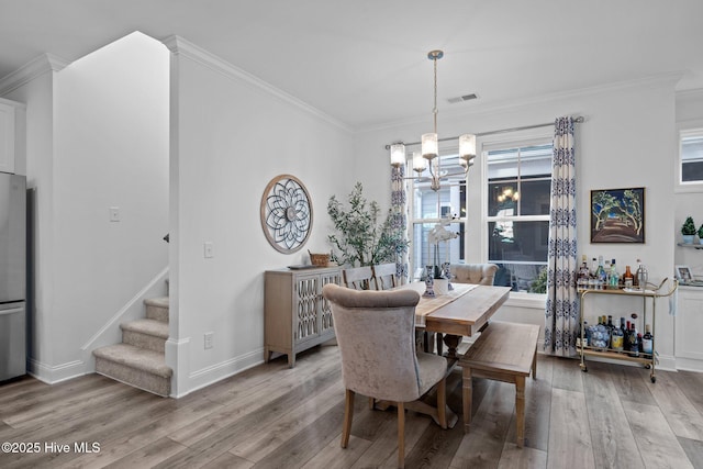 dining room with light wood finished floors, stairs, ornamental molding, and an inviting chandelier