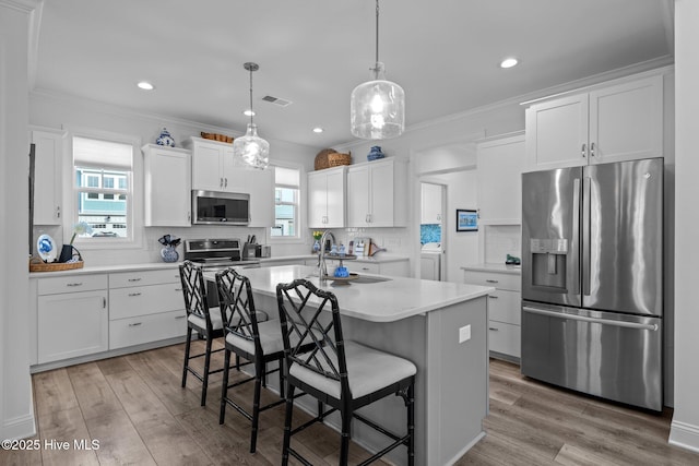 kitchen with appliances with stainless steel finishes, light countertops, a center island with sink, and white cabinetry