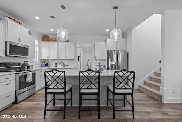 kitchen with stainless steel appliances, light countertops, decorative light fixtures, and an island with sink