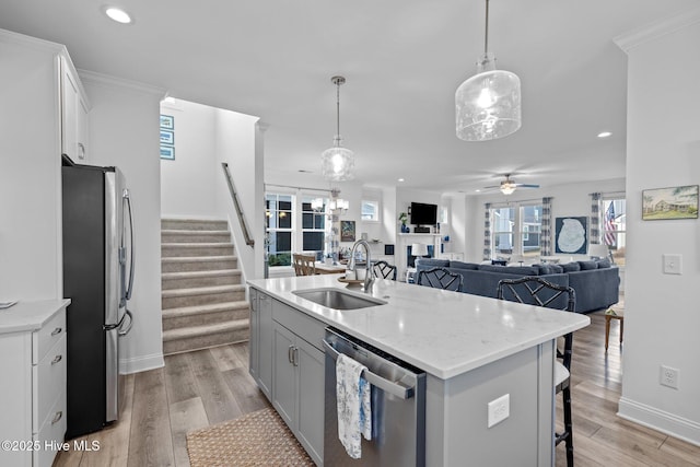 kitchen featuring a center island with sink, appliances with stainless steel finishes, open floor plan, hanging light fixtures, and a sink