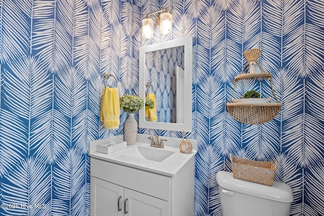 bathroom with vanity, toilet, and wallpapered walls