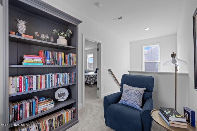 living area with an upstairs landing, plenty of natural light, visible vents, and light colored carpet