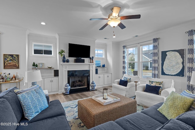 living area with a fireplace with raised hearth, ornamental molding, and light wood-type flooring