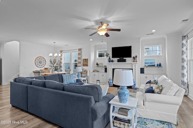 living area with a fireplace, visible vents, a wealth of natural light, light wood finished floors, and crown molding