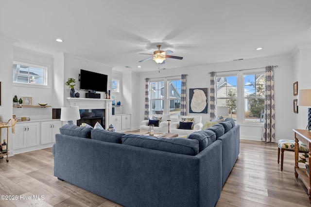 living area featuring light wood finished floors, baseboards, a ceiling fan, ornamental molding, and a fireplace