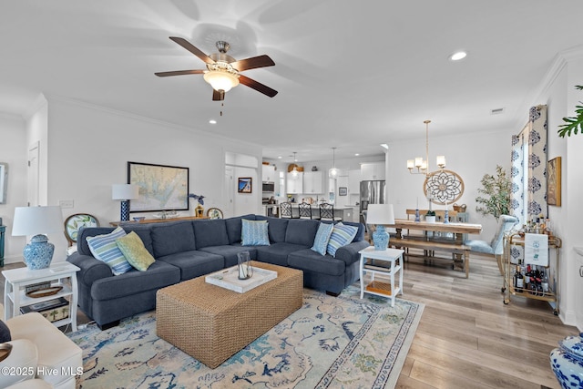 living room with ornamental molding, recessed lighting, light wood finished floors, and ceiling fan with notable chandelier