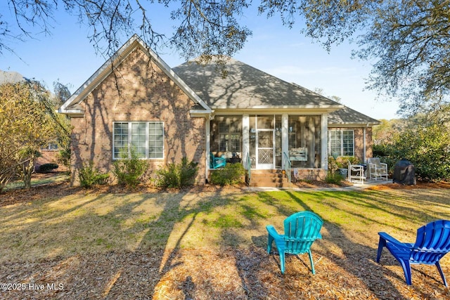 view of front of home featuring a front yard, brick siding, a sunroom, and a patio