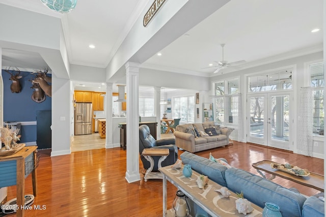living area with crown molding, baseboards, ceiling fan, decorative columns, and light wood-style flooring