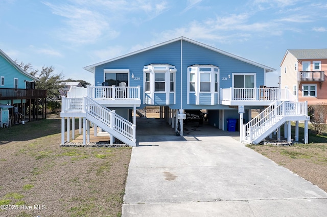 coastal inspired home with a carport, a porch, stairway, and concrete driveway