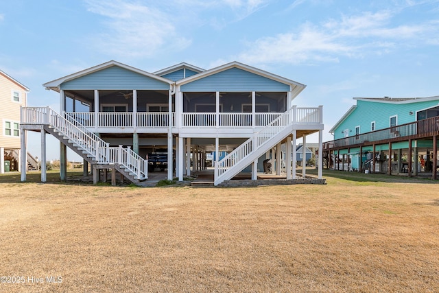 rear view of property featuring a ceiling fan, a sunroom, a yard, and stairs