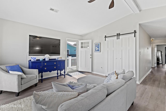 living area with a barn door, visible vents, a ceiling fan, lofted ceiling with beams, and wood finished floors