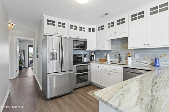 kitchen featuring white cabinets, light stone counters, stainless steel appliances, and a sink