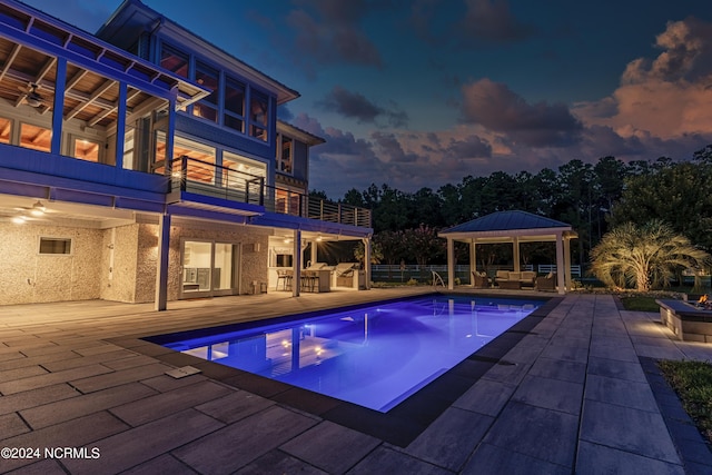 pool at dusk with a patio, an outdoor kitchen, an outdoor bar, an outdoor living space, and a gazebo