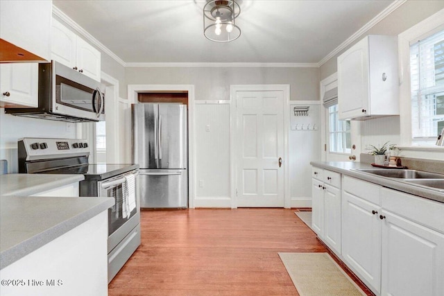 kitchen with appliances with stainless steel finishes, white cabinetry, sink, light hardwood / wood-style floors, and crown molding