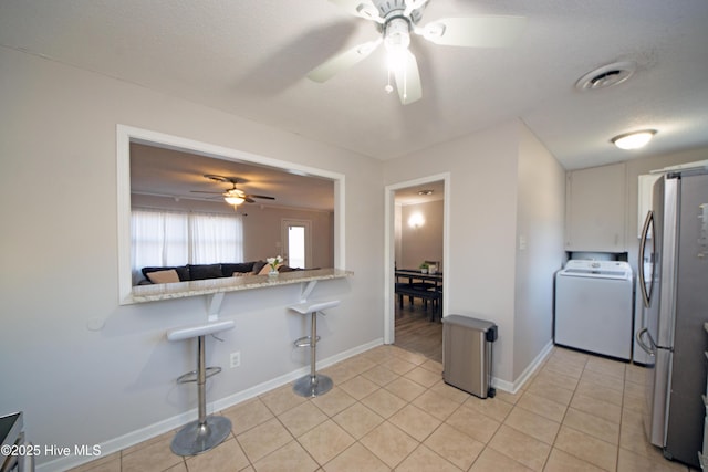 kitchen with a breakfast bar, washer / dryer, white cabinetry, stainless steel refrigerator, and kitchen peninsula