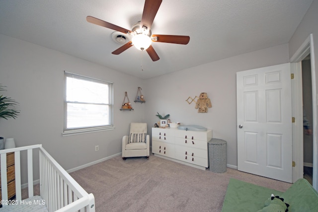 carpeted bedroom featuring ceiling fan, a textured ceiling, and a crib