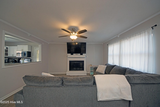 living room featuring ceiling fan, a large fireplace, ornamental molding, and hardwood / wood-style floors