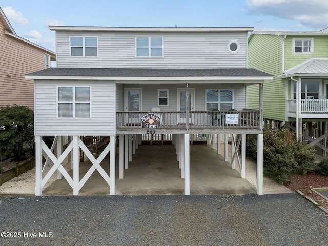 coastal inspired home featuring driveway, a shingled roof, a porch, and a carport