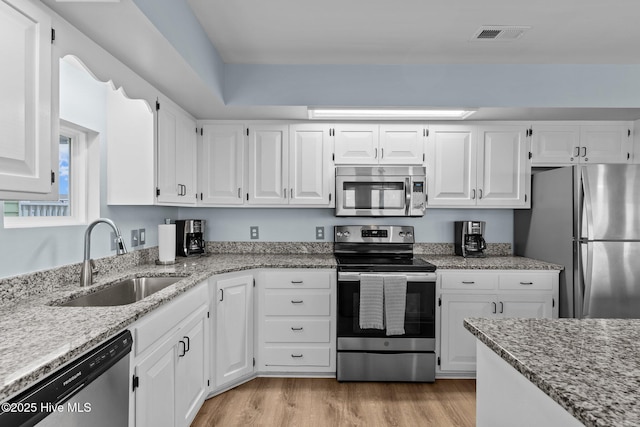 kitchen featuring stainless steel appliances, light wood finished floors, white cabinetry, and a sink