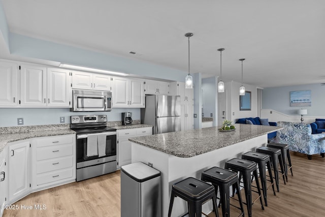 kitchen featuring open floor plan, a center island, white cabinets, and appliances with stainless steel finishes