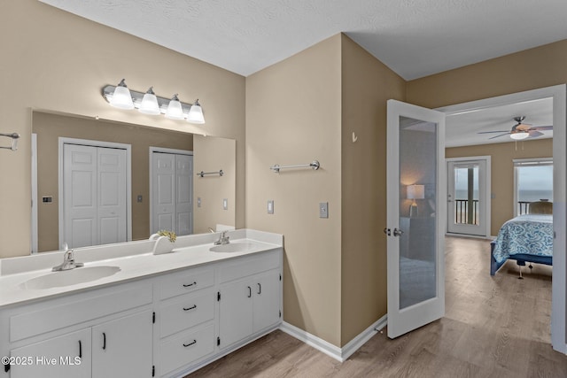 ensuite bathroom featuring a sink, a closet, double vanity, and wood finished floors