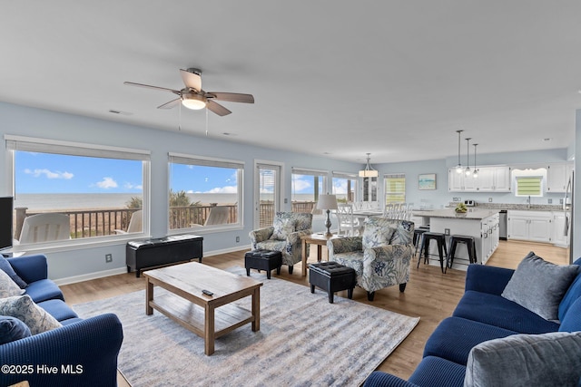 living area featuring baseboards, a ceiling fan, light wood-style flooring, and a water view