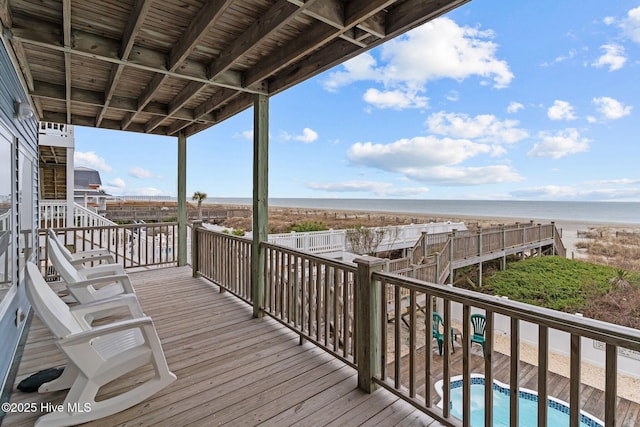 deck featuring a beach view, stairs, a water view, and an outdoor pool