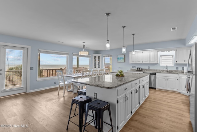 kitchen with visible vents, a kitchen island, white cabinetry, stone counters, and light wood-style floors