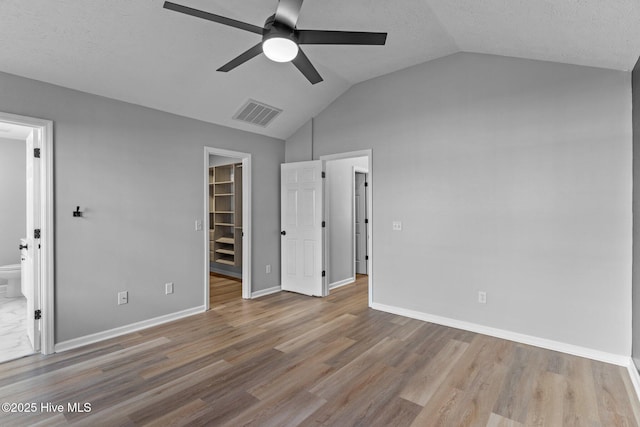 unfurnished bedroom with light hardwood / wood-style flooring, a closet, a spacious closet, lofted ceiling, and ensuite bathroom