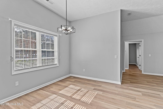 empty room featuring light hardwood / wood-style flooring, a chandelier, and a textured ceiling