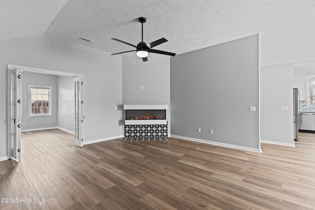 unfurnished living room featuring ceiling fan, lofted ceiling, wood-type flooring, and a textured ceiling