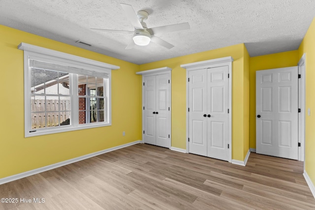 unfurnished bedroom with ceiling fan, multiple closets, light hardwood / wood-style floors, and a textured ceiling