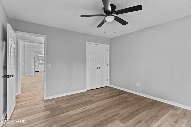 unfurnished bedroom with light hardwood / wood-style floors, a closet, ceiling fan, and a textured ceiling