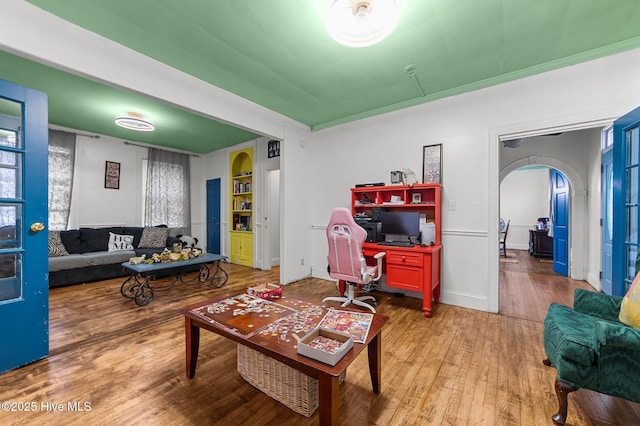 living area featuring arched walkways, baseboards, and wood finished floors