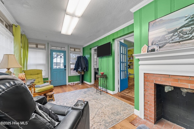 living room featuring light wood finished floors, baseboards, ornamental molding, a textured ceiling, and a brick fireplace