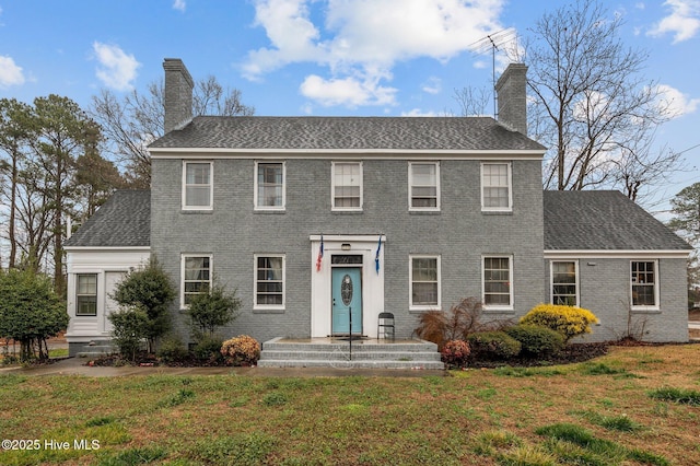 colonial-style house featuring brick siding, a chimney, and a front lawn