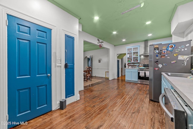 kitchen with light wood finished floors, white cabinets, wall chimney exhaust hood, stainless steel appliances, and light countertops